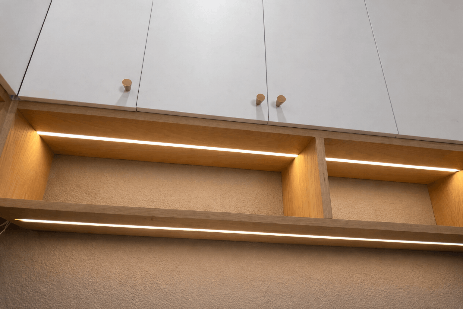 Wooden shelves with built-in warm LED lighting under white cabinets.