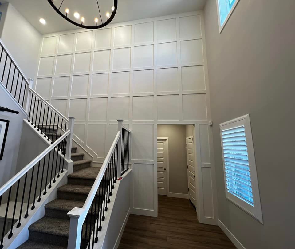 Two-story entryway with staircase, white paneling, and doorframes in a home.