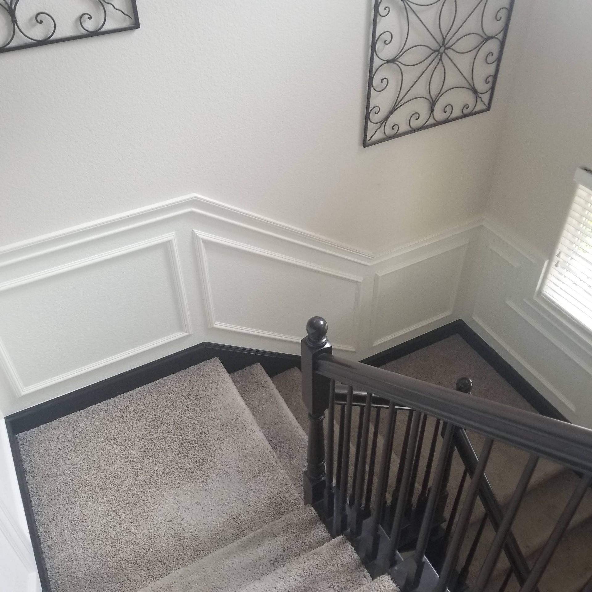 Staircase with gray carpet, black railing, and white walls with decorative molding. Two decorative metal wall hangings.