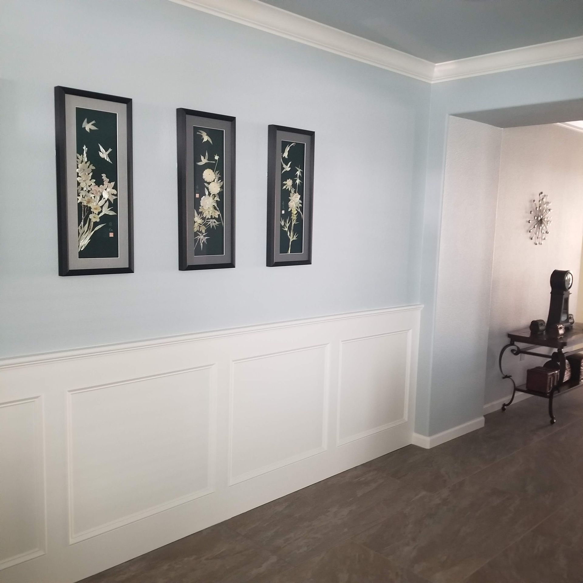 A hallway with light blue walls, white wainscoting, and three framed pictures.
