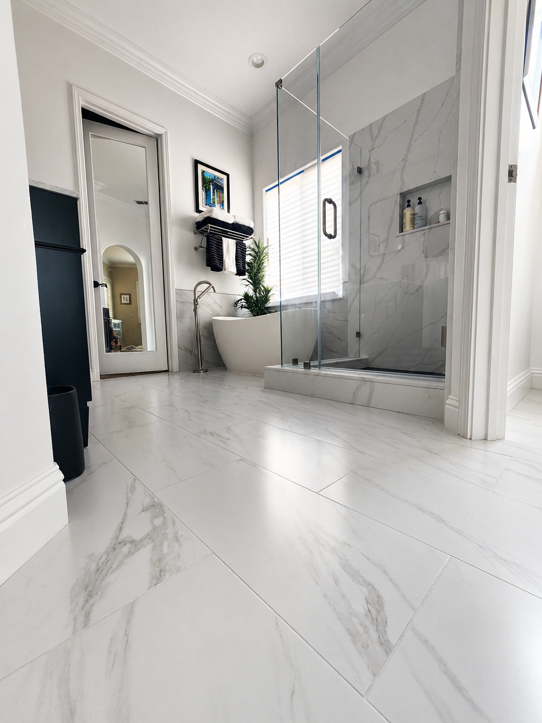 Modern bathroom with marble-look tile floor, glass shower, white tub, and tall mirror.