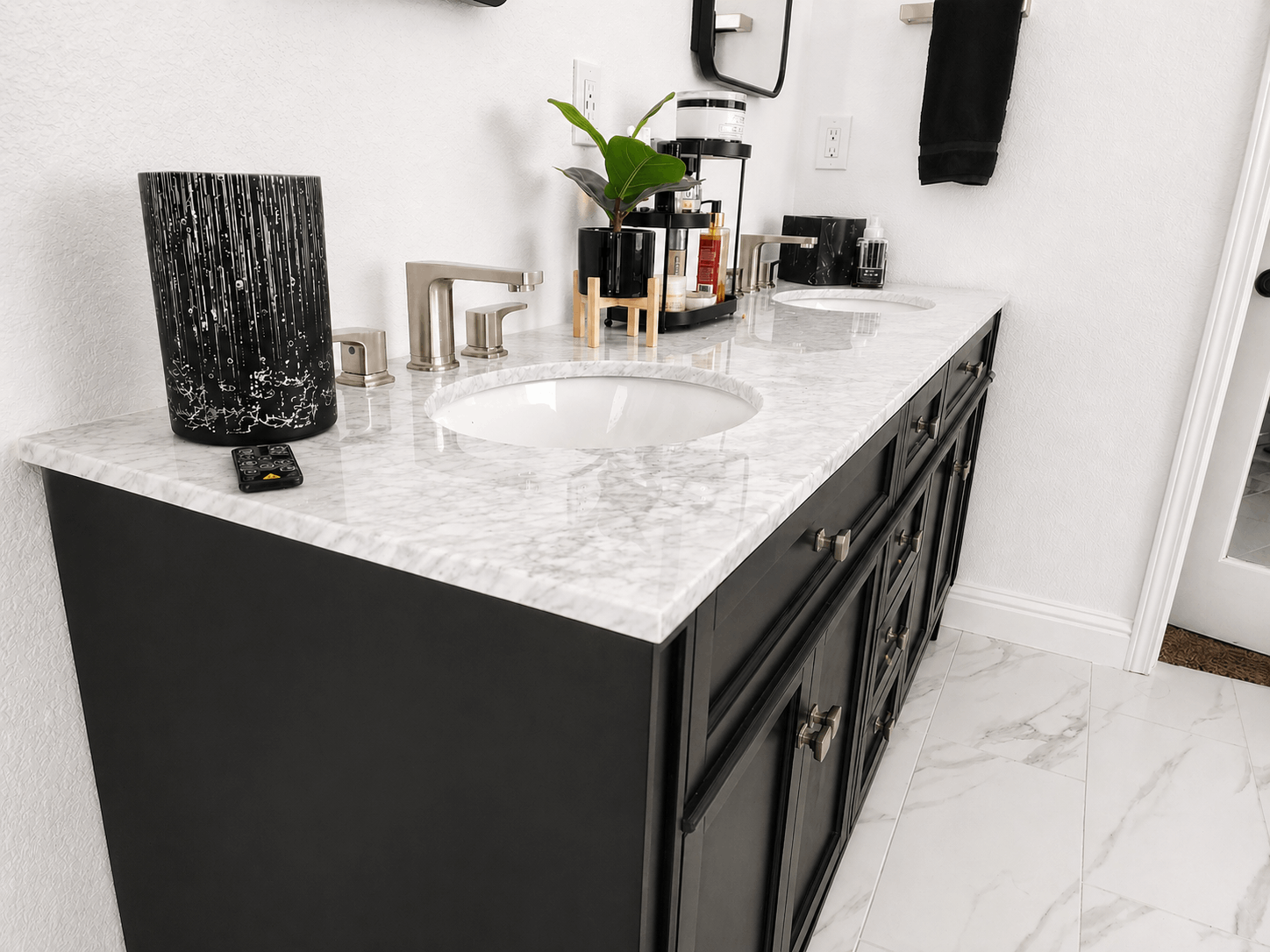 Modern bathroom vanity with black cabinets, marble countertop, dual sinks, and a decorative tray with toiletries