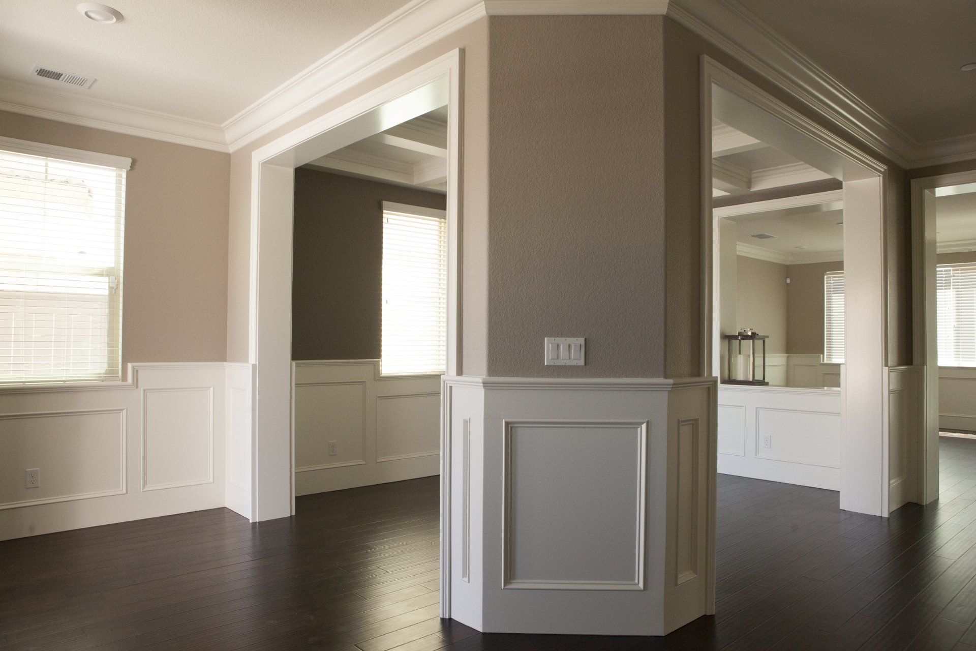 Interior view of a corner with dark floors, white trim, and beige walls separating rooms.