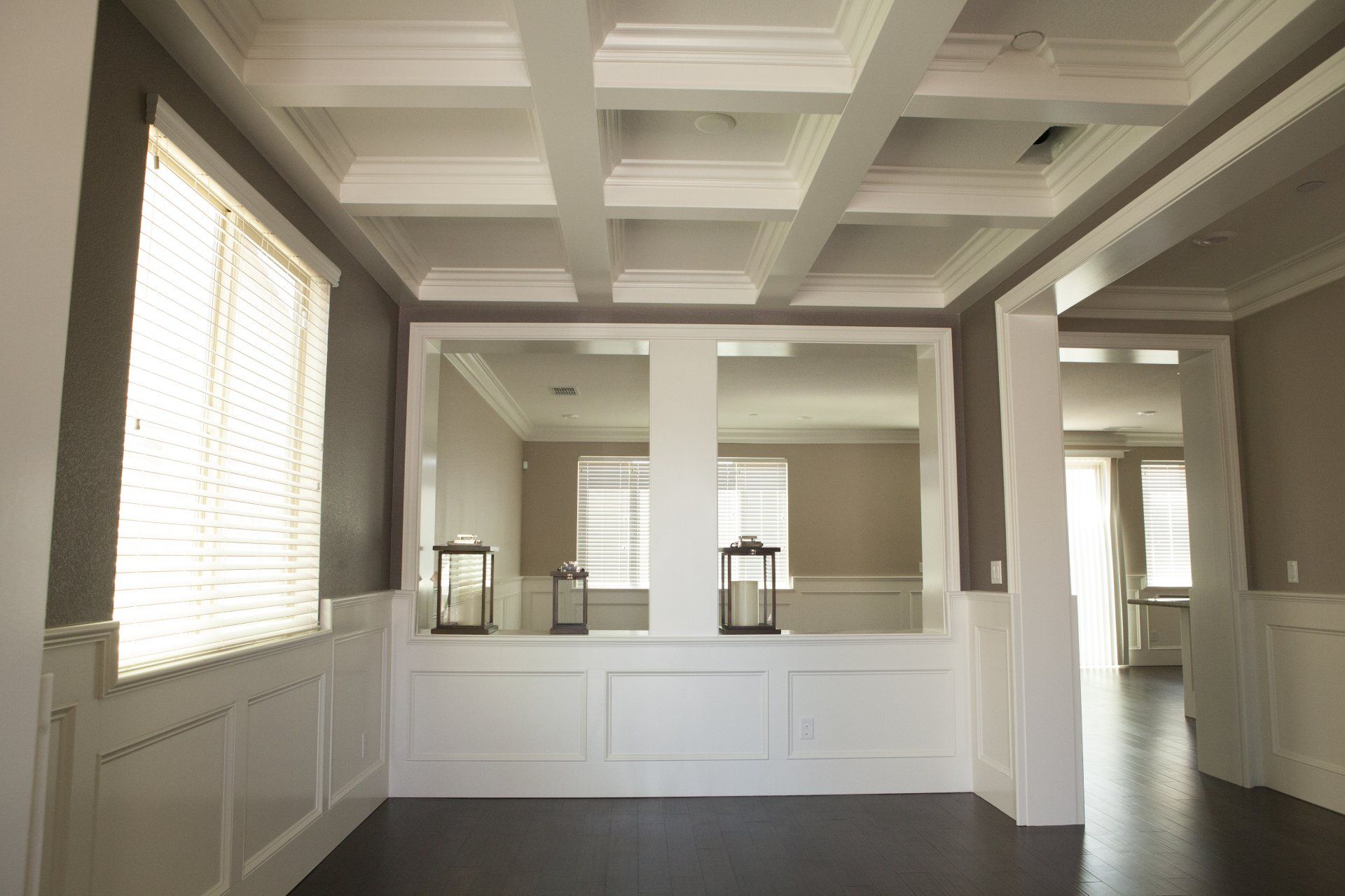 Formal dining room with white paneled walls and ceiling beams, dark floors, and large mirror.