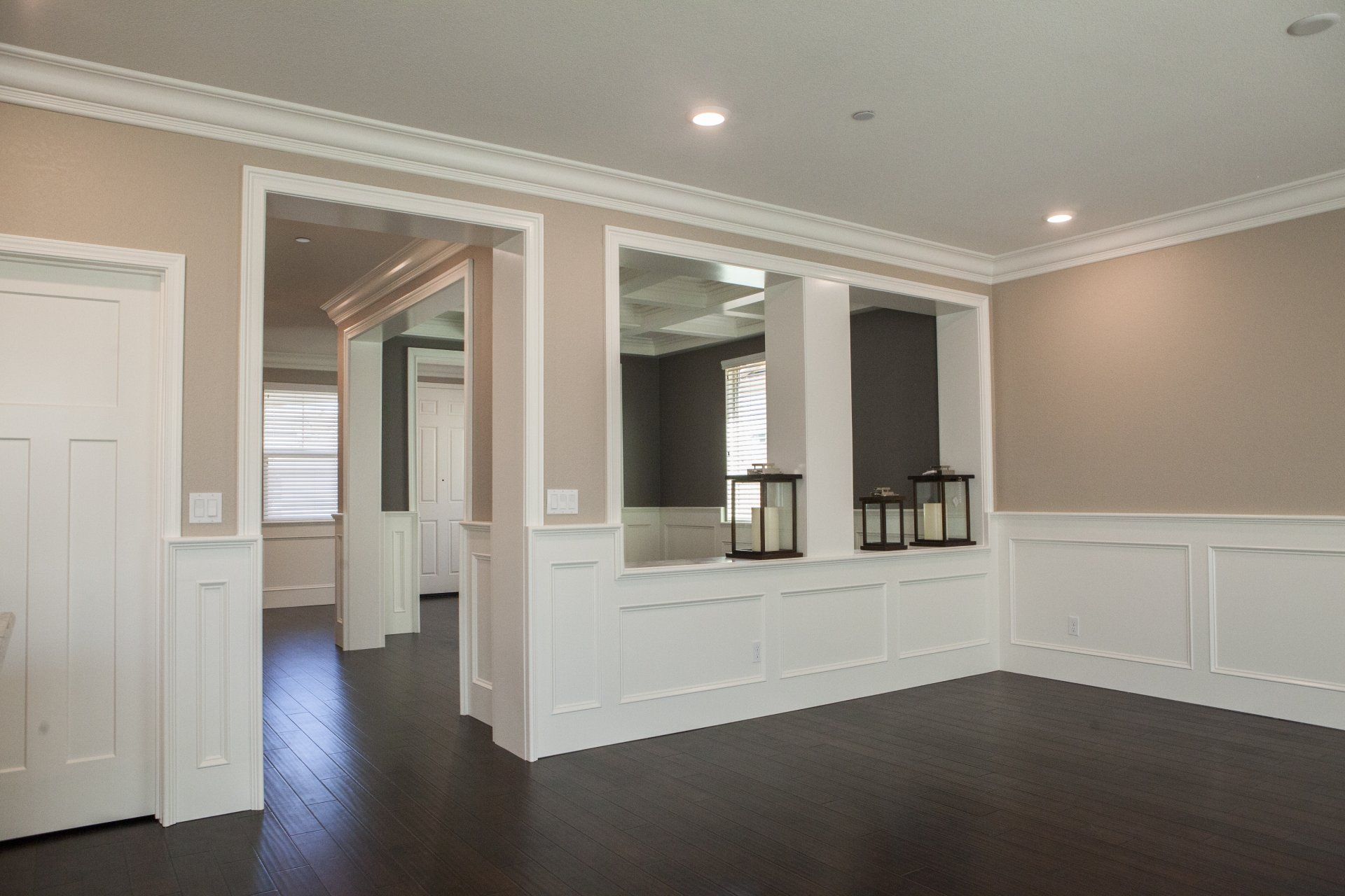 Empty dining room with dark wood floor, tan walls, and white paneling.
