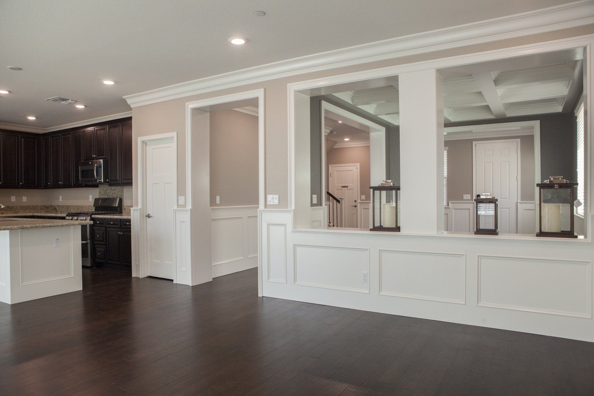 Living area with dark wood floors, white paneling, kitchen visible on the left, large mirrors on the wall.