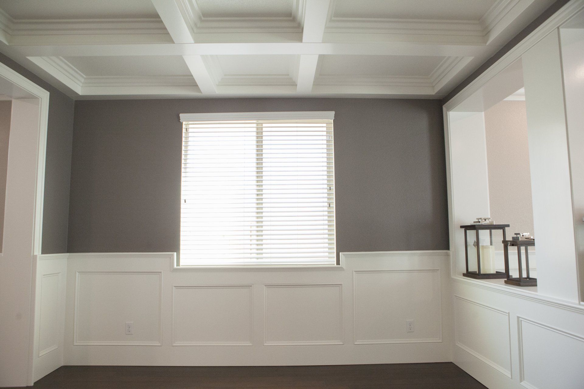 Empty room with gray walls, white trim, and coffered ceiling; a window with blinds.