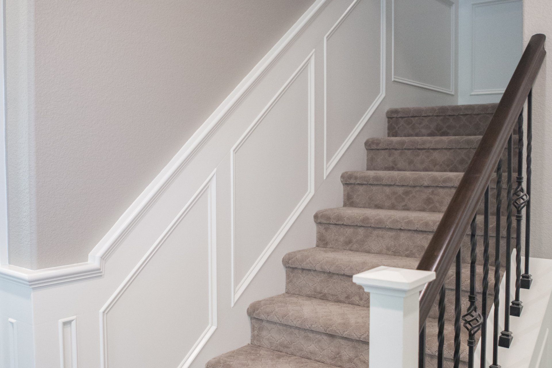 Staircase with carpet, white trim, and dark brown handrail. Wall has decorative white panels and light grey wallpaper.