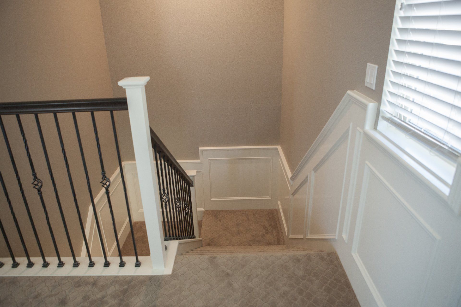 Staircase with black railing and white trim leading downward; carpeted floor and tan walls.
