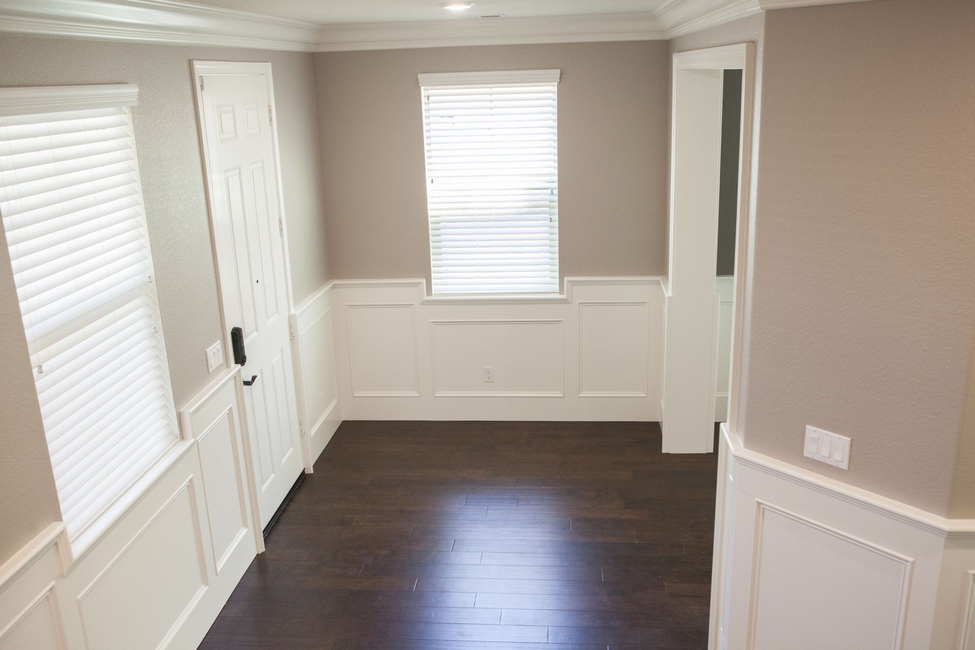 Empty room with wood floors, wainscoting, and blinds; neutral-colored walls.