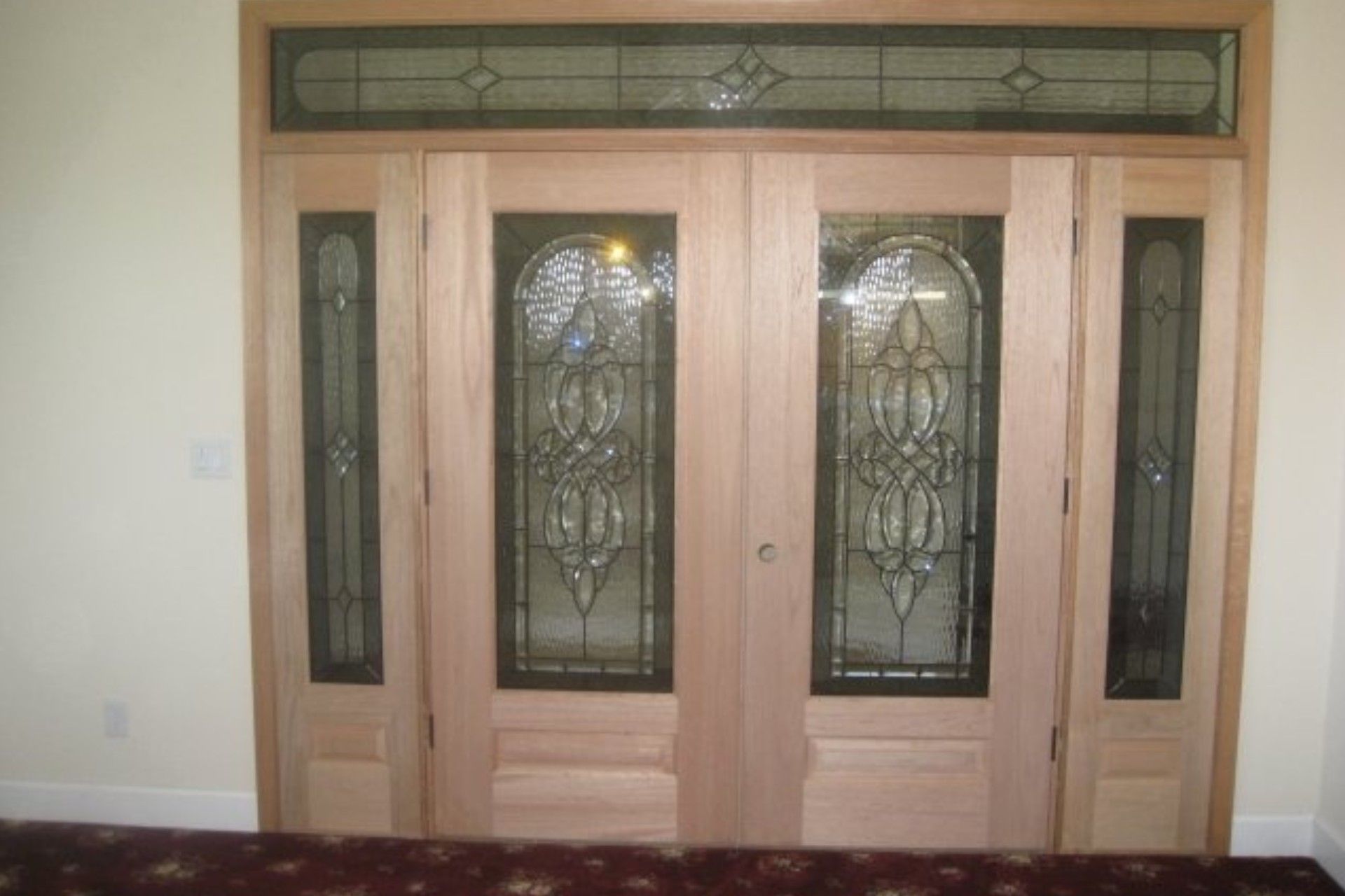 Double wooden entry doors with stained glass and sidelights, topped by a stained glass transom.
