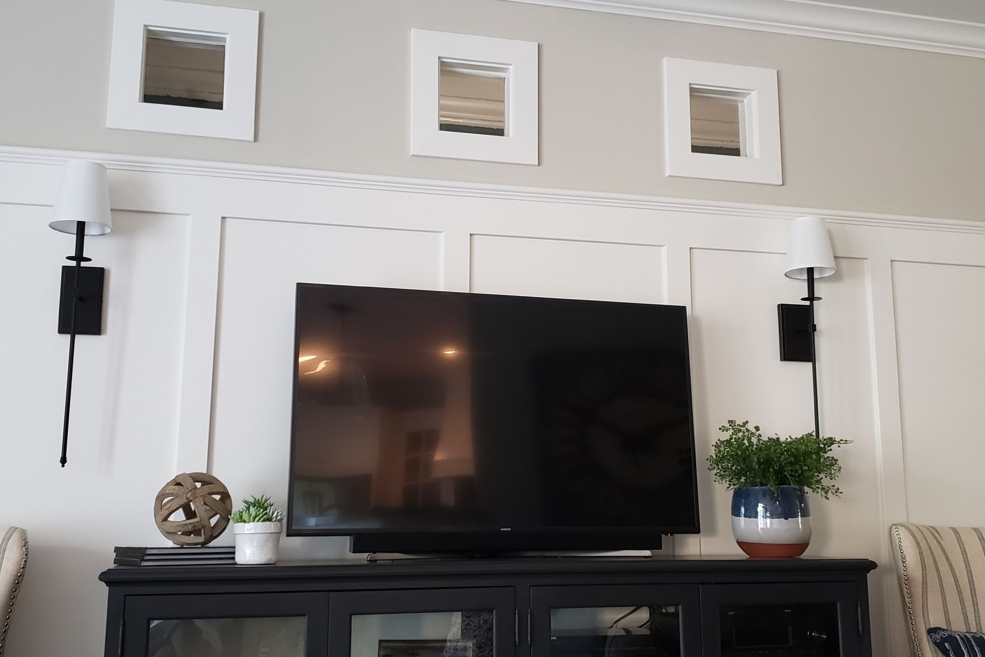 Living room with TV on a black cabinet, flanked by sconces and three framed mirrors above.