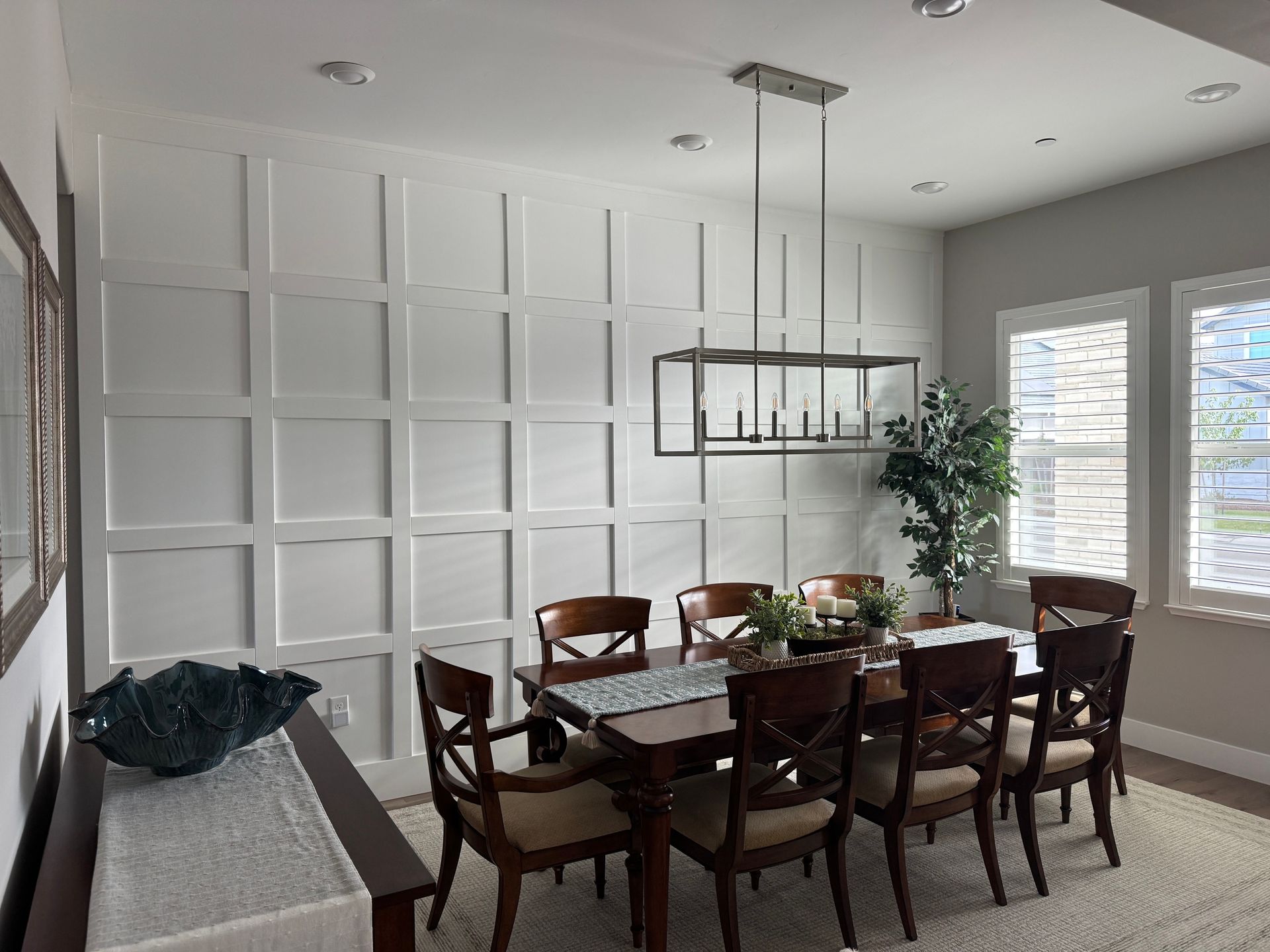 Modern dining room with a dark wood table, white paneled wall, and a hanging black light fixture