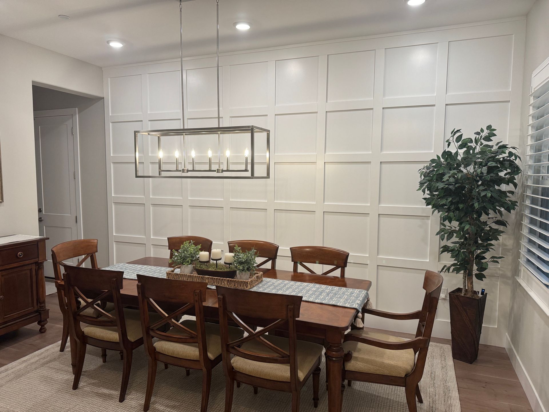 Elegant dining room with a long wooden table, upholstered chairs, pendant light, and white paneled wall