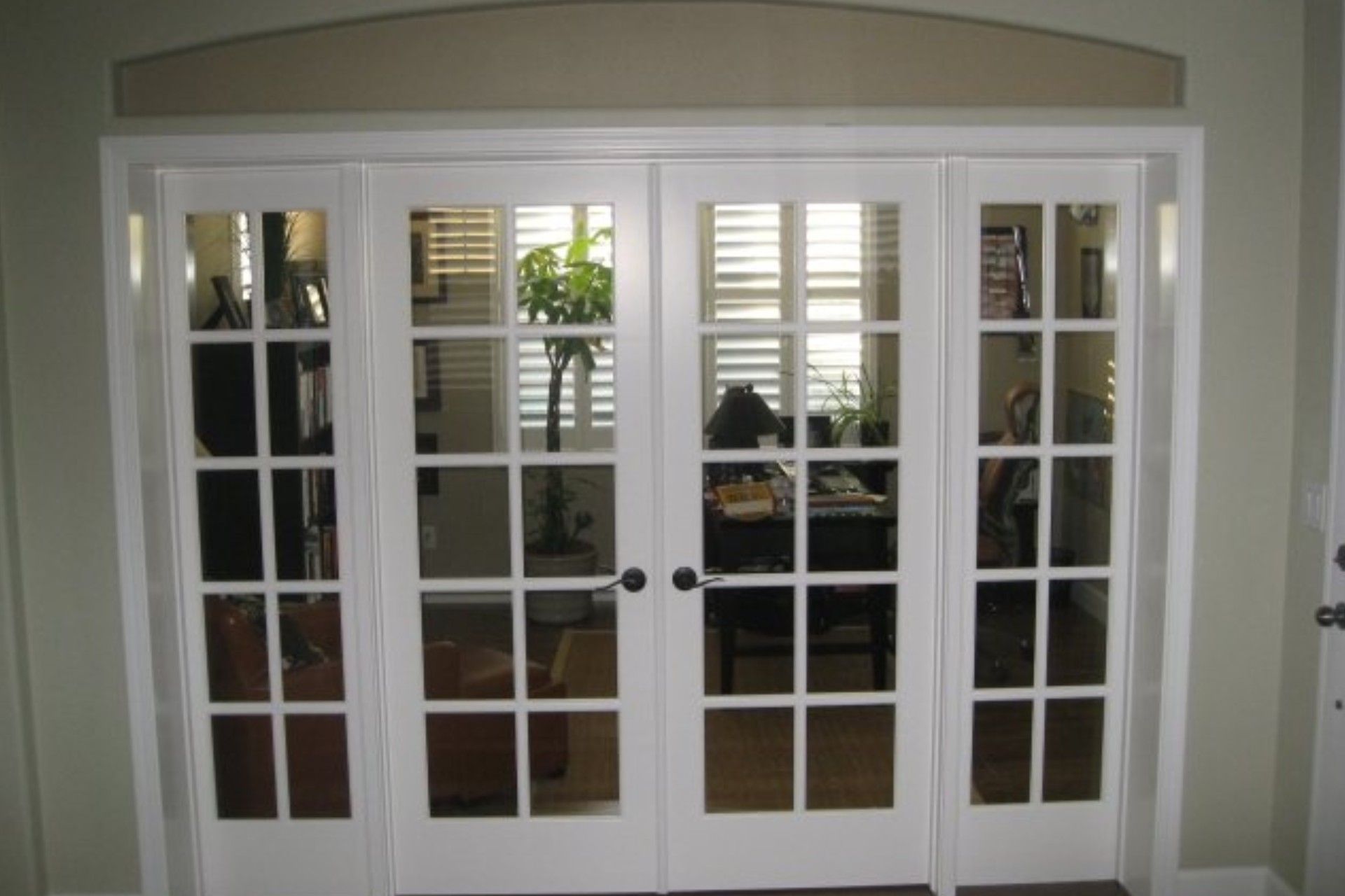 White French doors with glass panes, arched top, view into a room with sunlight.