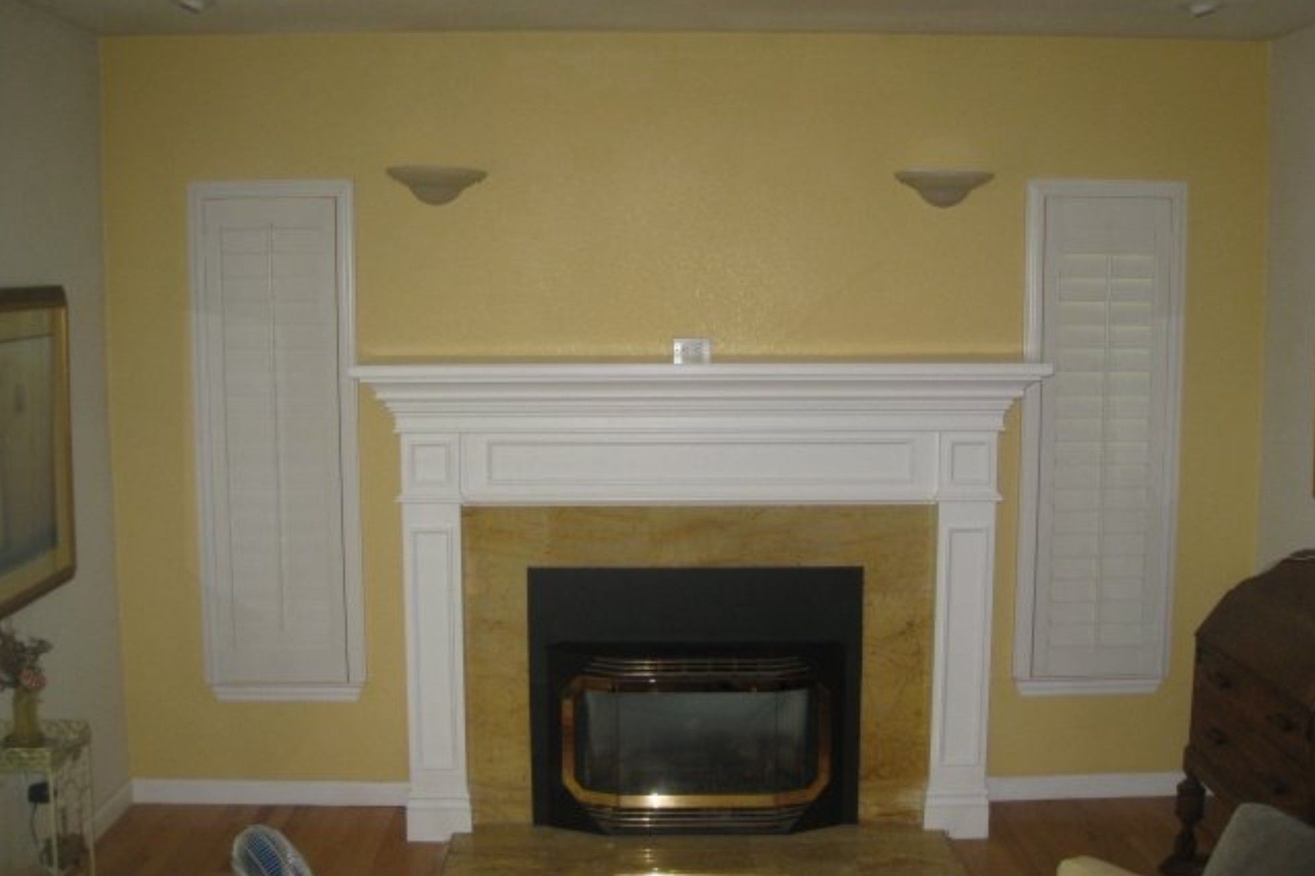 Yellow-walled room with a white fireplace, marble facing, and shuttered storage.