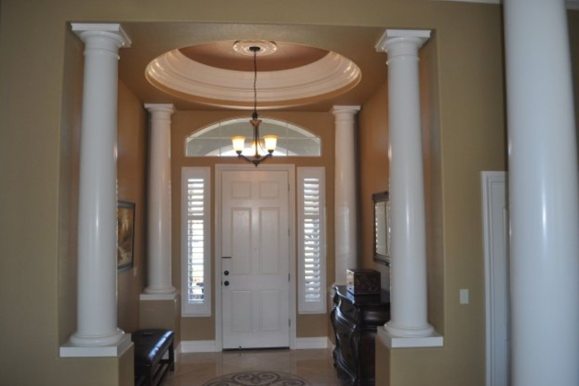 Grand entryway with white columns, arched doorway, and chandelier.