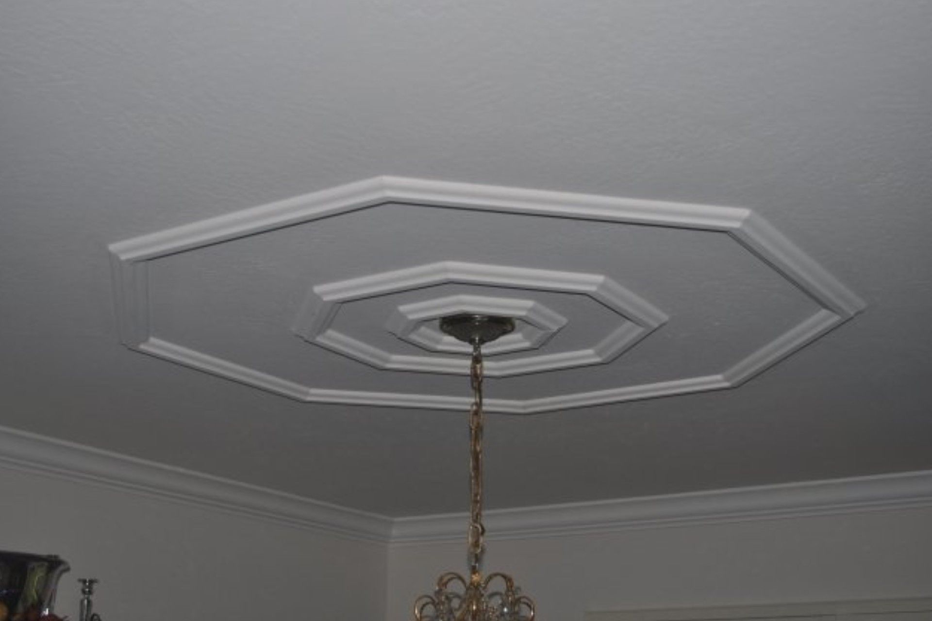White ceiling with octagonal decorative molding around a chandelier.