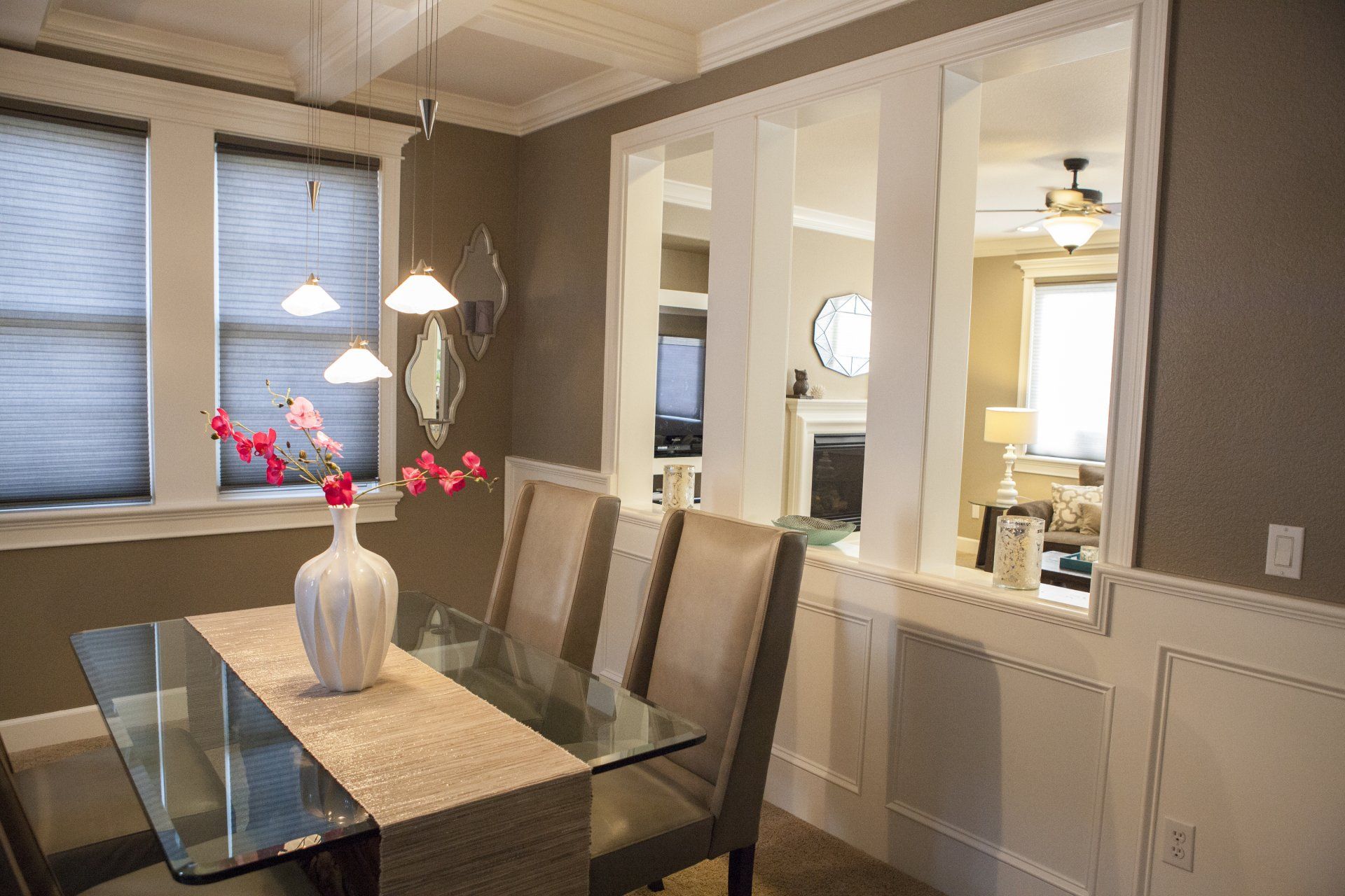 Dining room with glass table, chairs, and a view into another room through pillars.