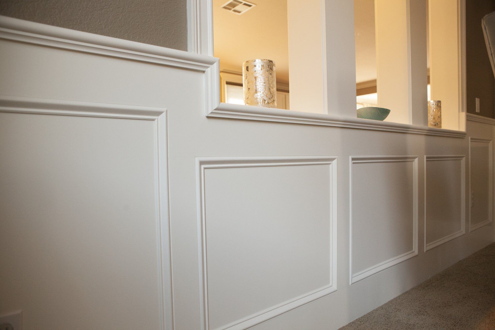 White wainscoting with square panels and molding in a home's interior, with a glimpse of another room.
