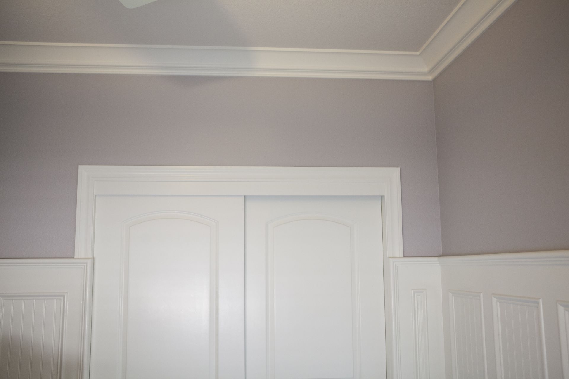White closet doors with white trim against lavender walls and crown molding.
