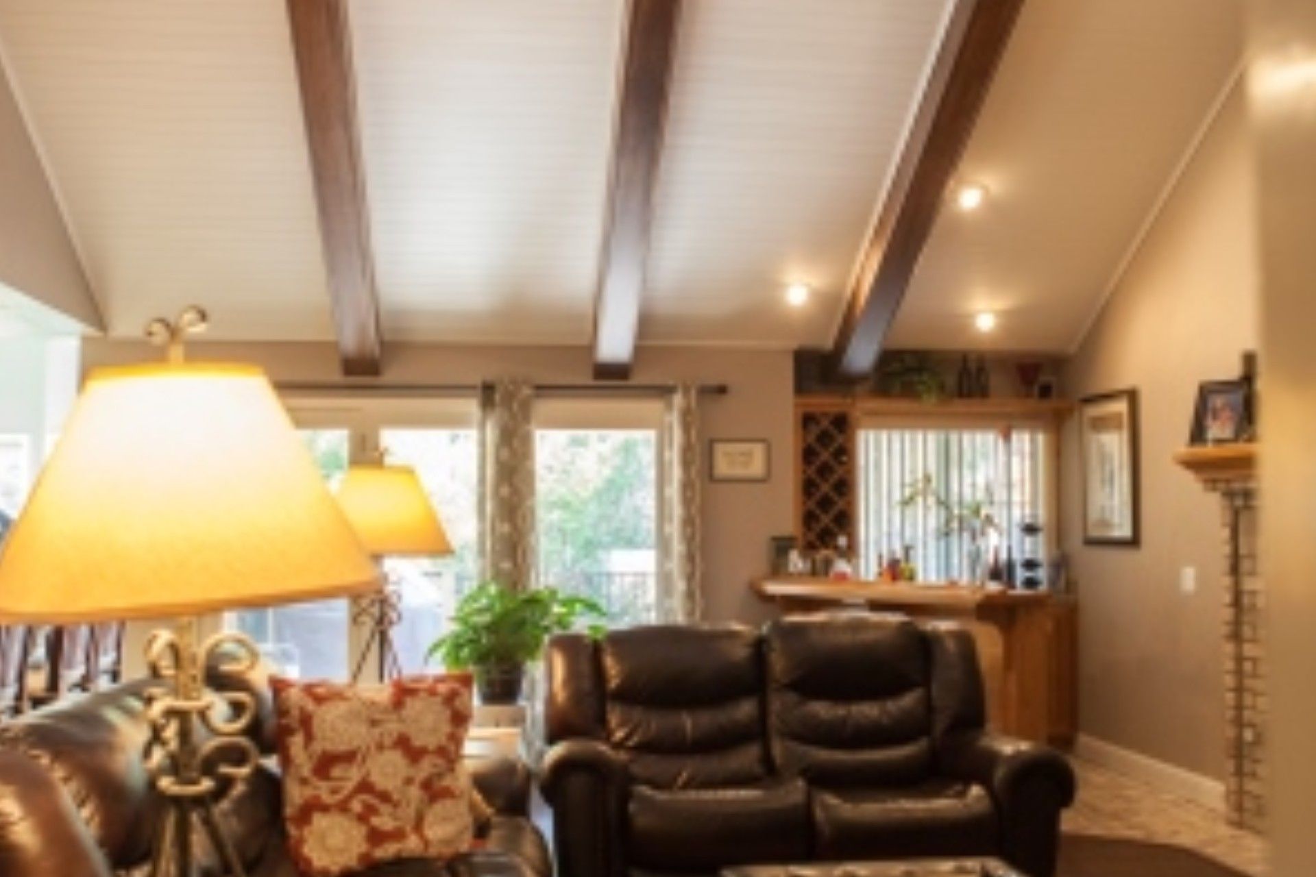 Living room with brown beams, leather furniture, bar, and windows.