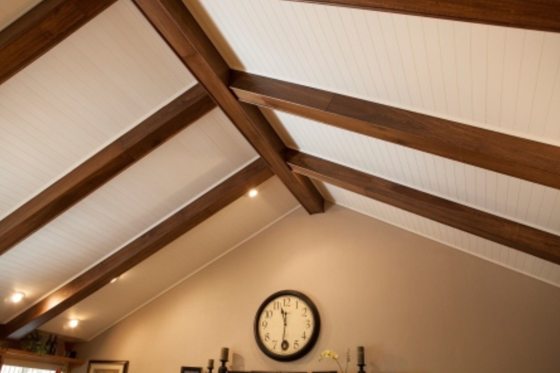 Beamed, vaulted ceiling with white panels and dark wood beams; large clock on a tan wall.