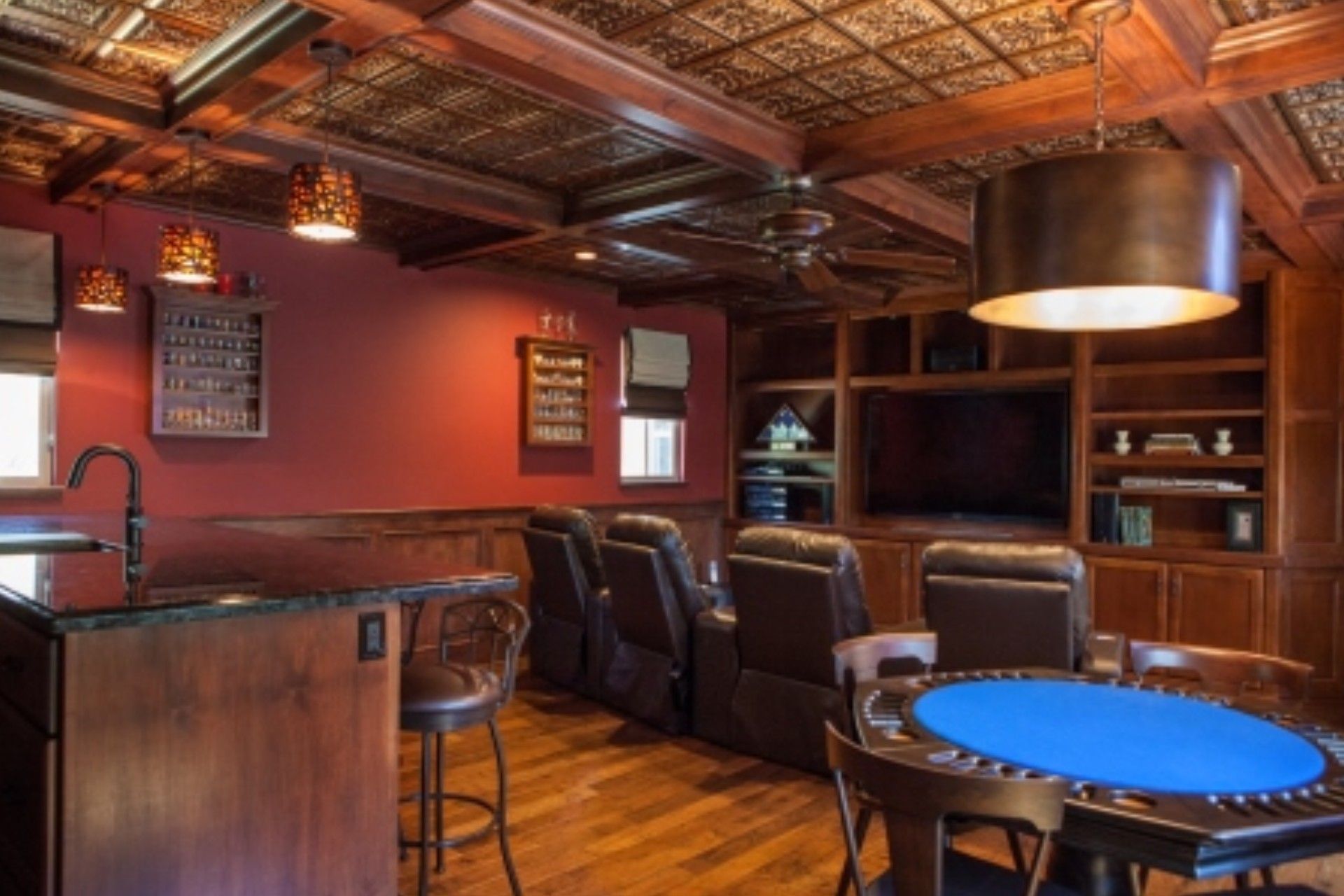 A cozy den with red walls, a bar, a home theater, and a poker table.