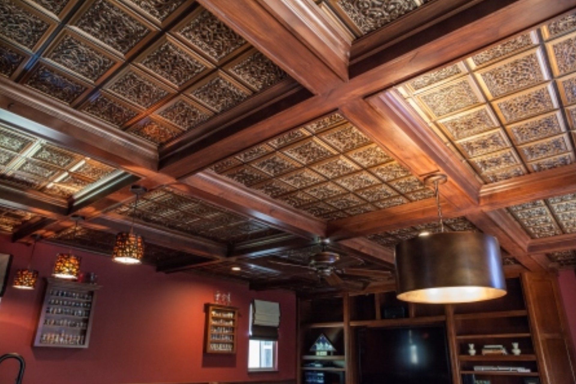Ornate copper-toned ceiling tiles and dark wood beams in a room with red walls, pendant lights, and built-in shelving.