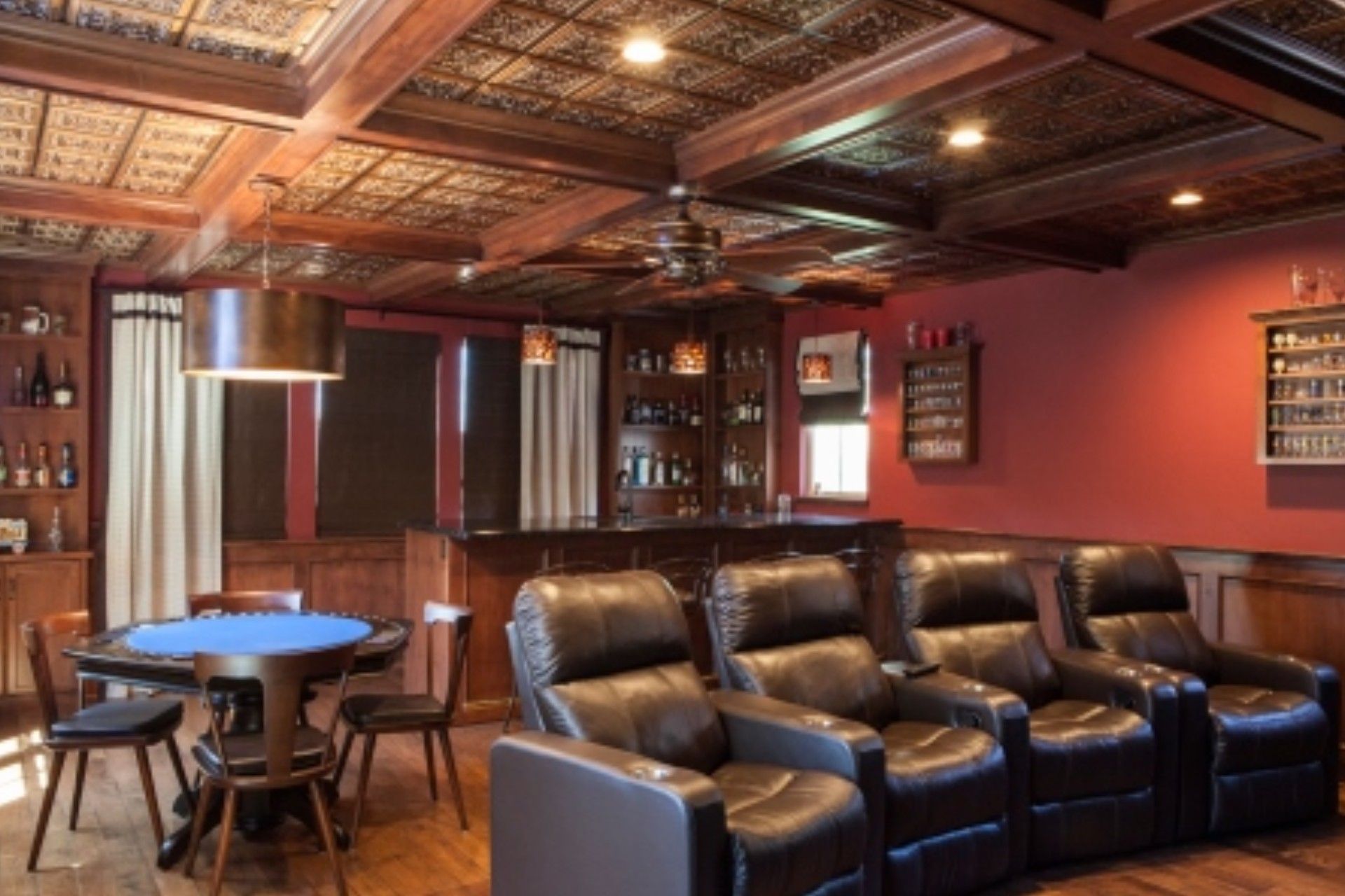 A home bar and theater room with a poker table, reclining chairs, and wooden ceiling.