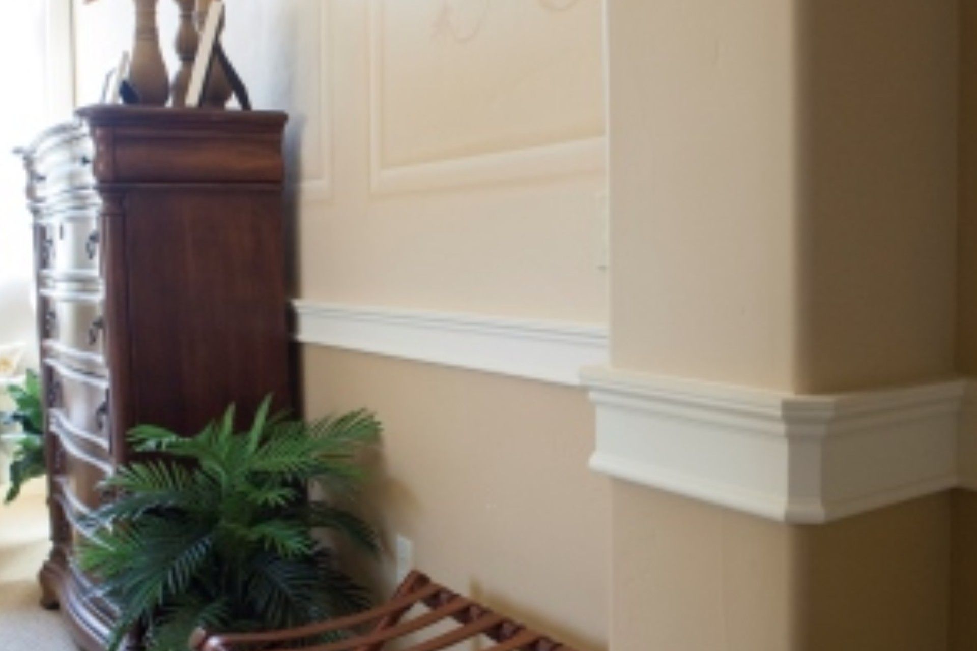 Corner of a room with beige walls, white molding, and a wooden dresser.