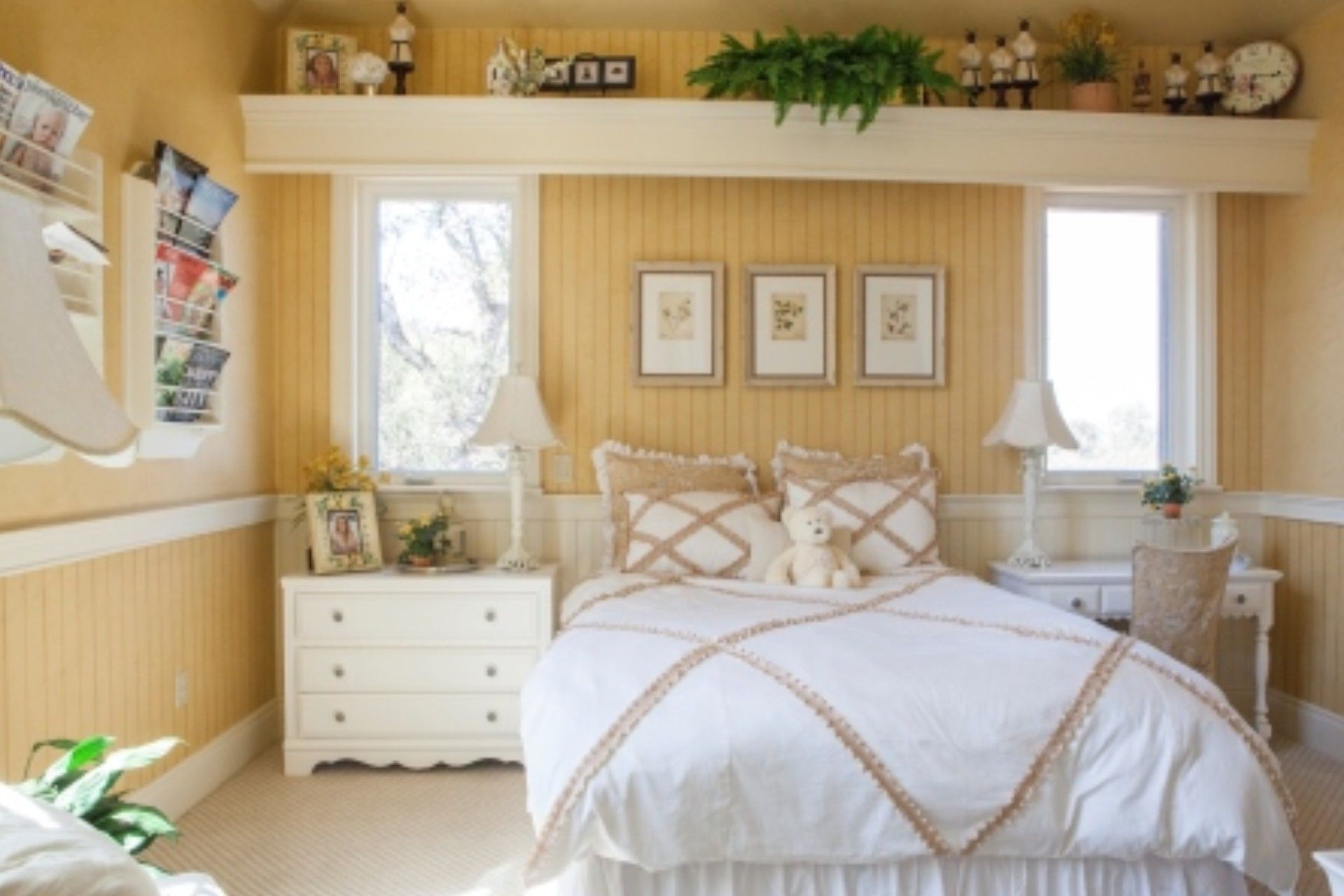 Cozy bedroom with yellow walls, white furniture, and a bed. Three framed pictures hang above the bed.
