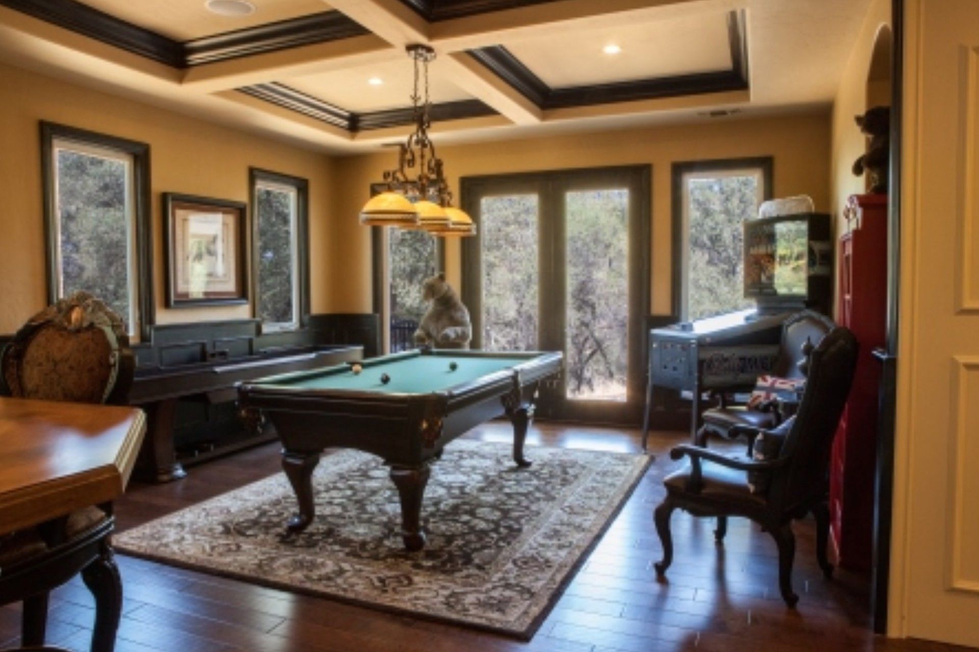 Billiard room: pool table on patterned rug, black accents, chandelier, windows to outside.