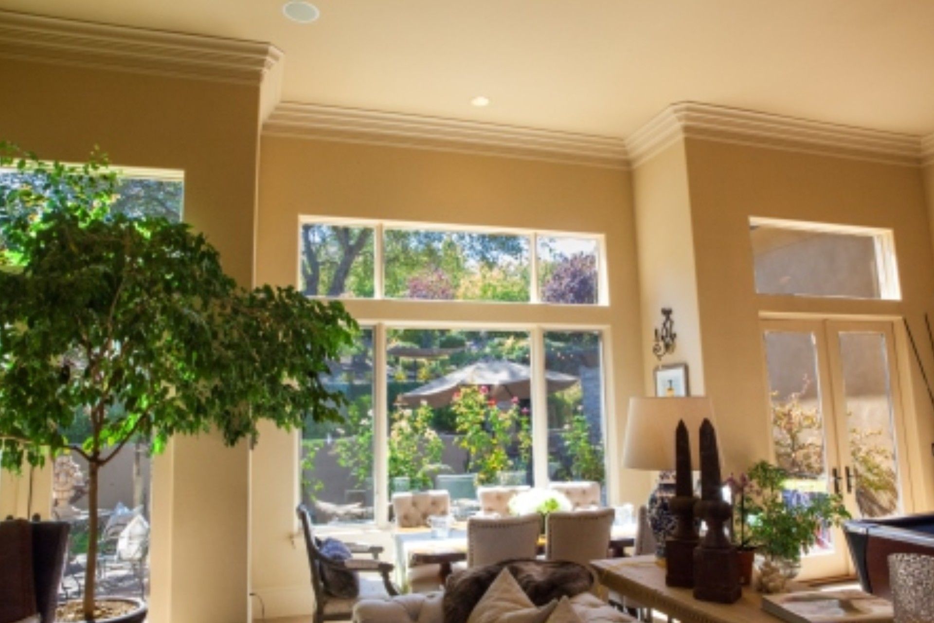 Living room with large windows, tree, tan walls, and outdoor view of a garden.
