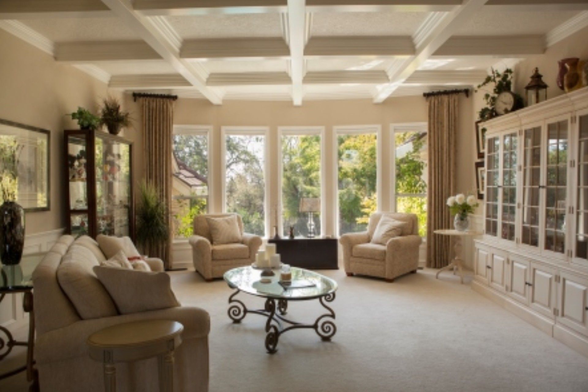 Bright living room with ivory furniture, large windows, and a coffered ceiling.