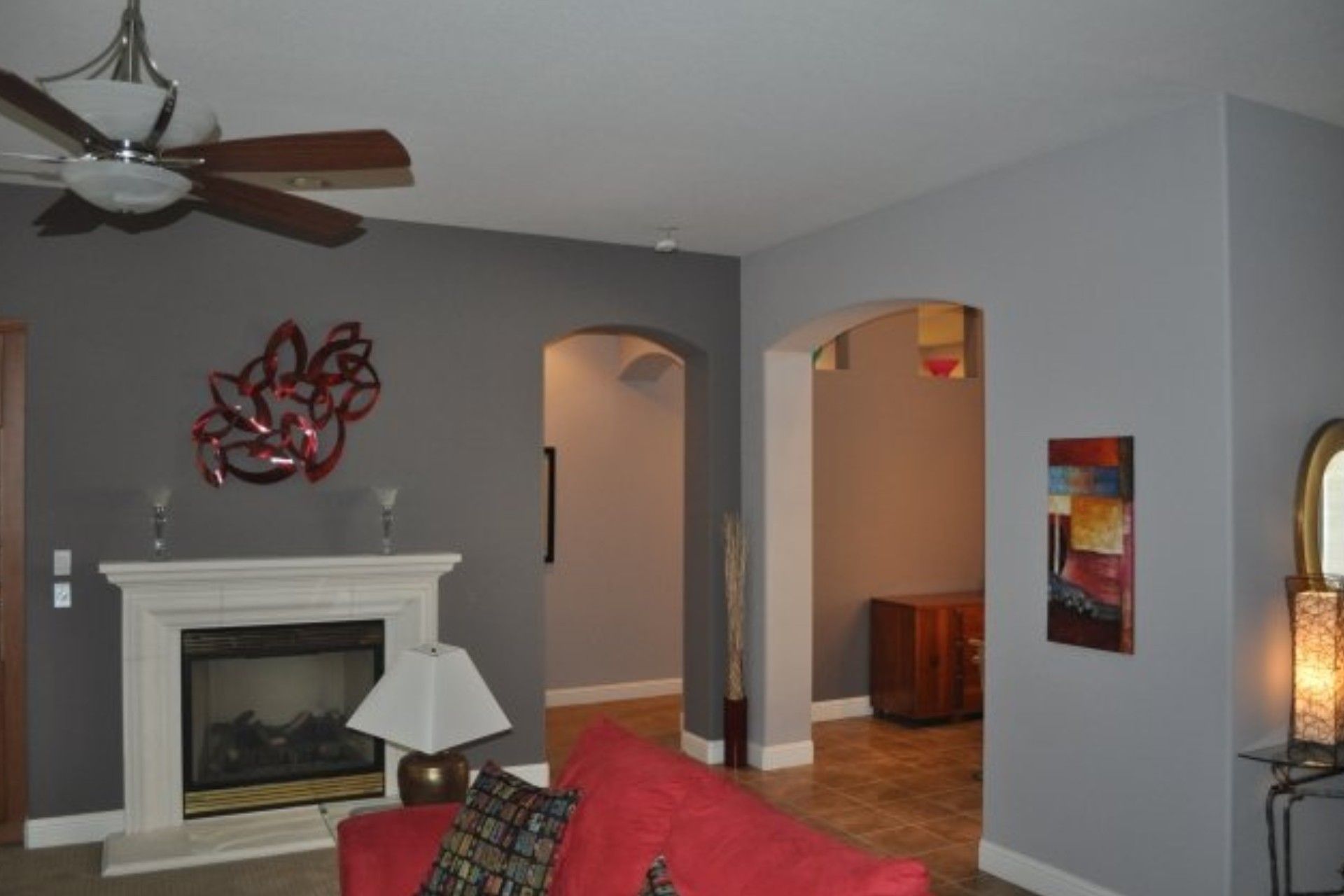 Living room with gray walls, white fireplace, archways, and abstract art. A red couch is visible.