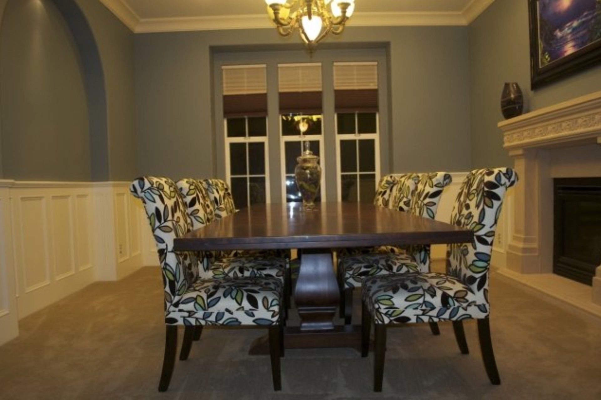 Dining room with floral upholstered chairs, wooden table, fireplace, and window.
