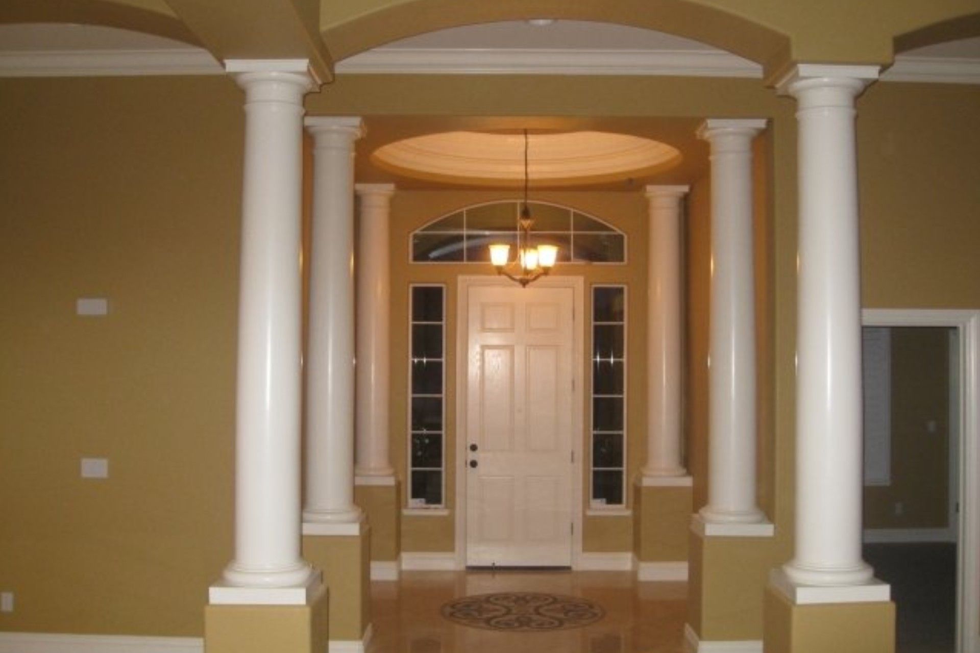 Entryway with white columns, arched doorway, a white door, and chandelier.
