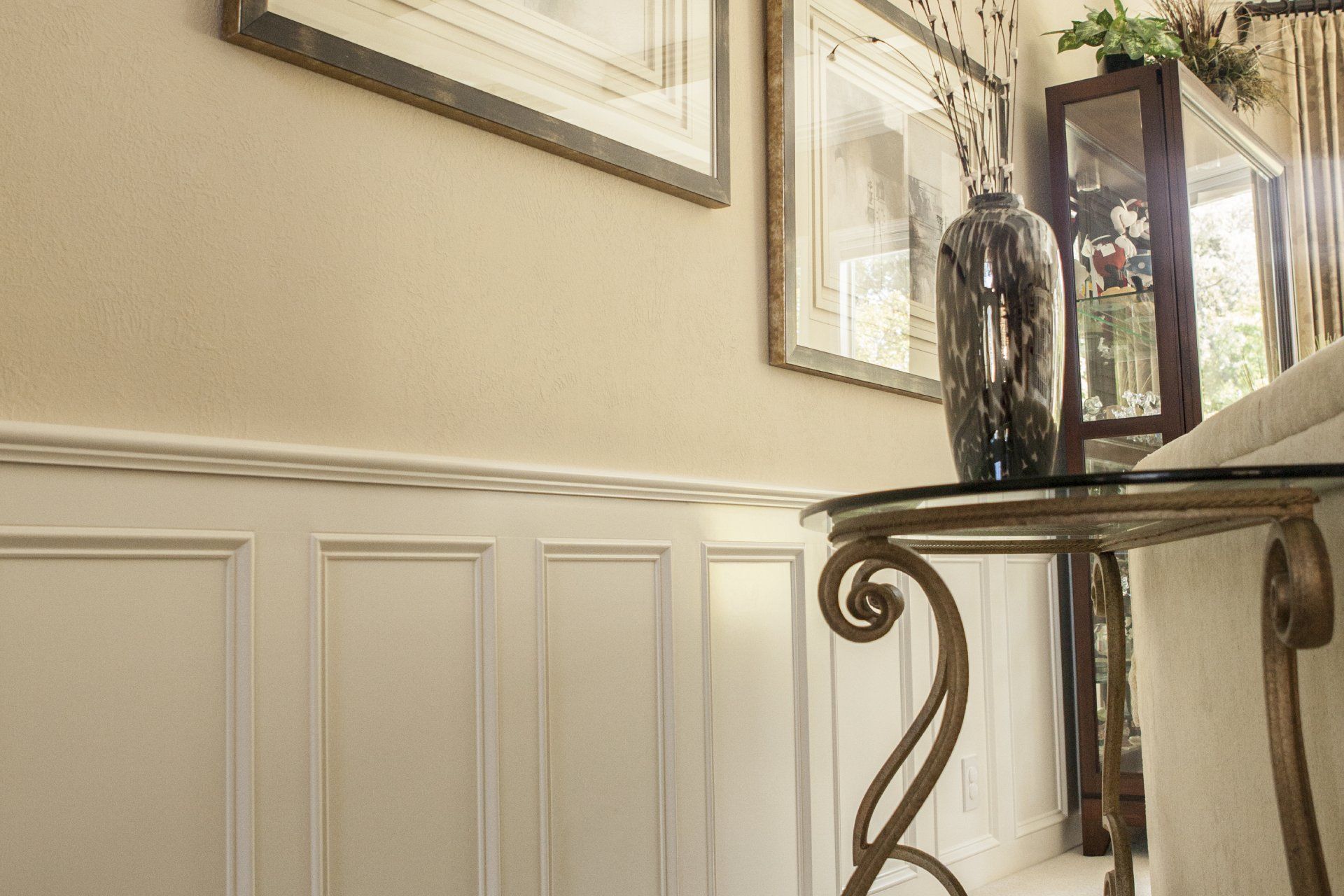 Beige room with wainscoting, framed artwork, and a decorative table with a vase.