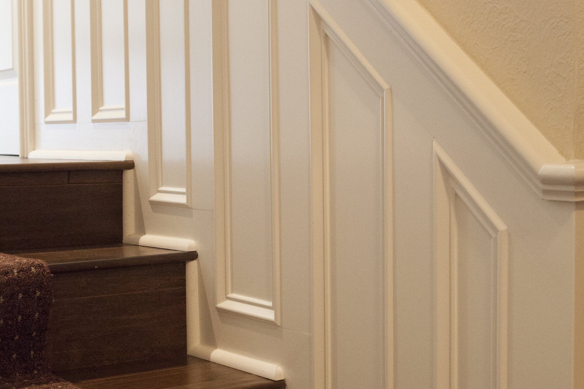 Staircase with white wainscoting and dark wooden steps. Includes a tan wall and brown carpet on the steps.