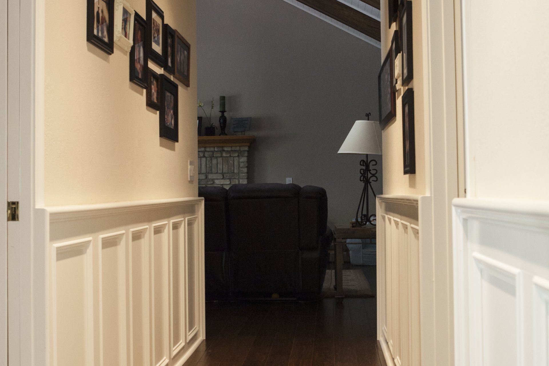 Hallway leading to a living room with a fireplace, framed photos, and white wainscoting.