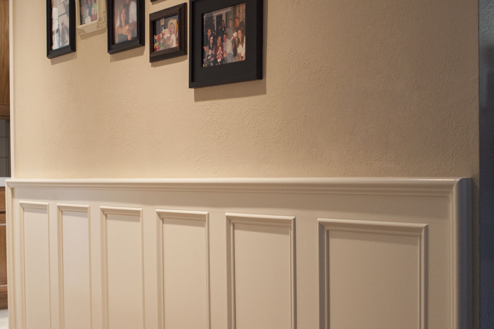 Beige wainscoting on a tan wall, with framed photos above.