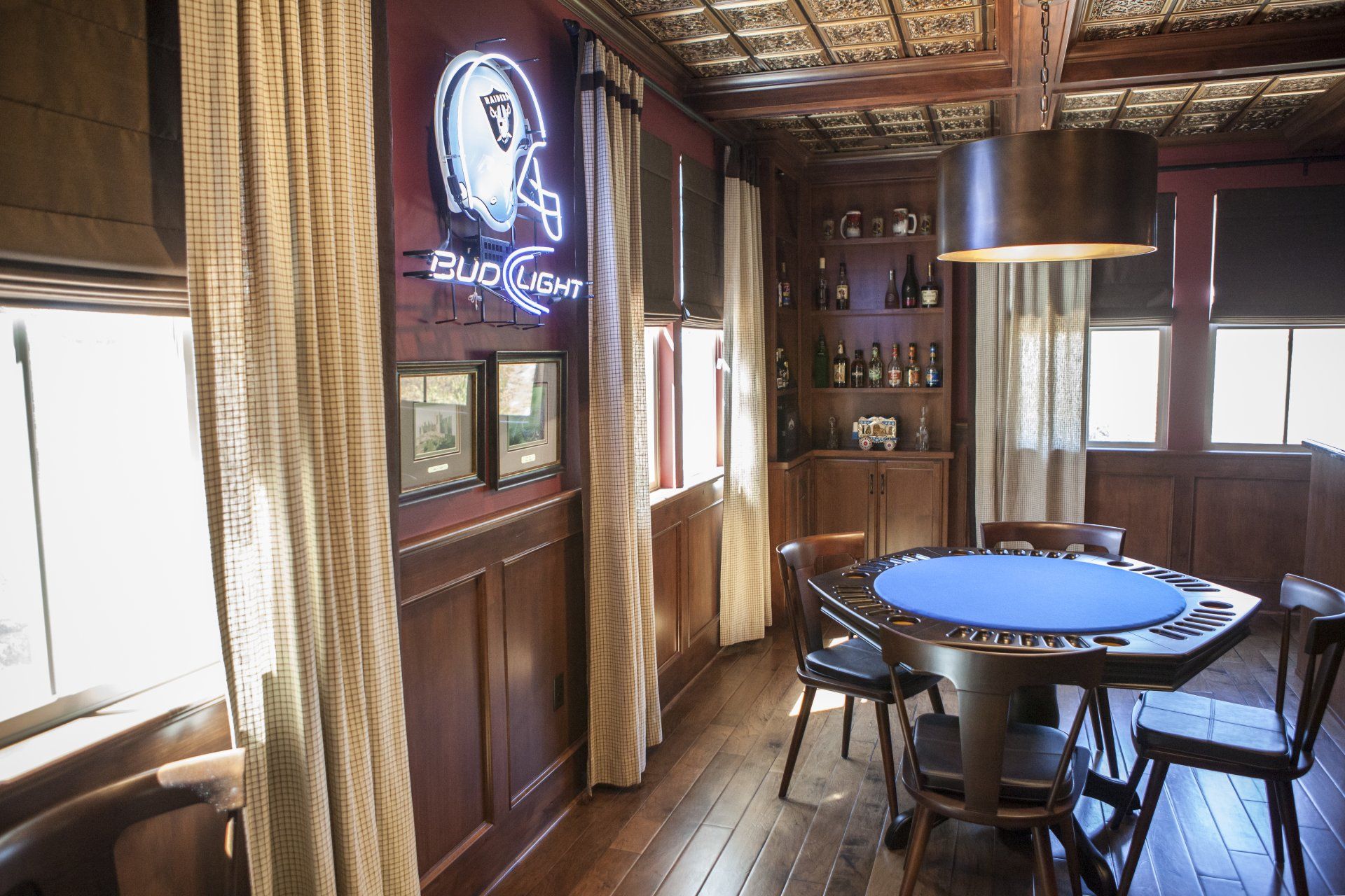 Game room with a poker table, bar, and neon sign on a wooden wall.