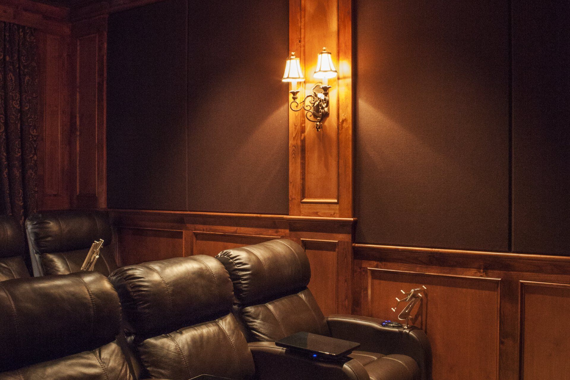Home theater with dark recliner seats and wood paneling, sconce lighting.