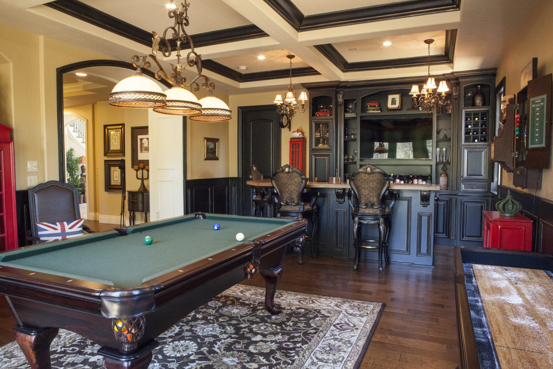 A game room with a pool table, bar, dark cabinets, and chairs.