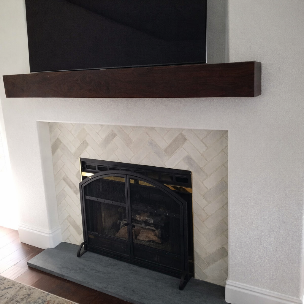 Fireplace with a black screen above it, dark wood mantel, herringbone tile, and black fire screen.