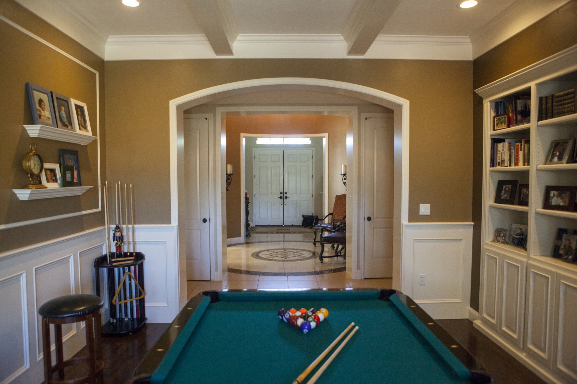 Pool table in a room with bookshelves, archway to entrance, and brown walls.