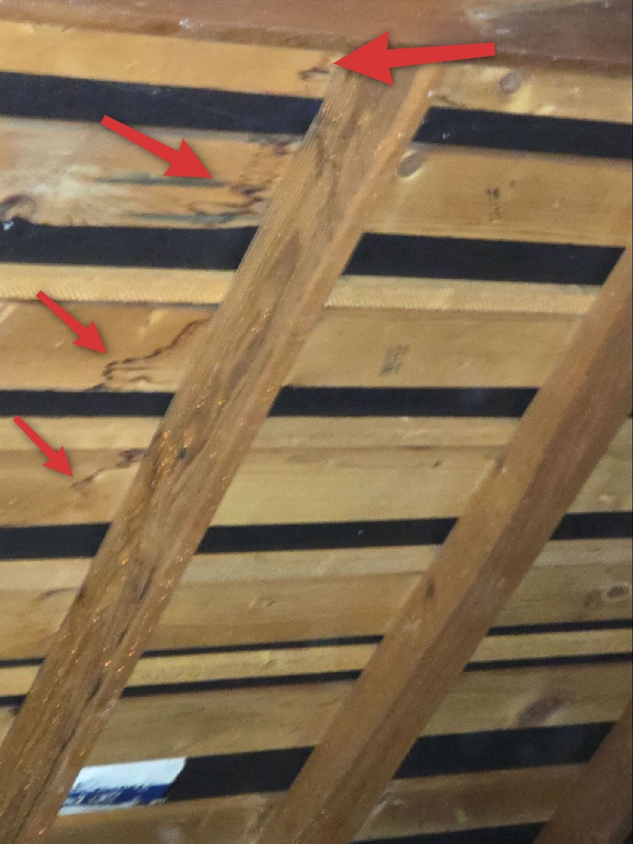 Attic roof rafters and wooden boards showing signs of moisture damage, indicated by dark staining and red arrows.