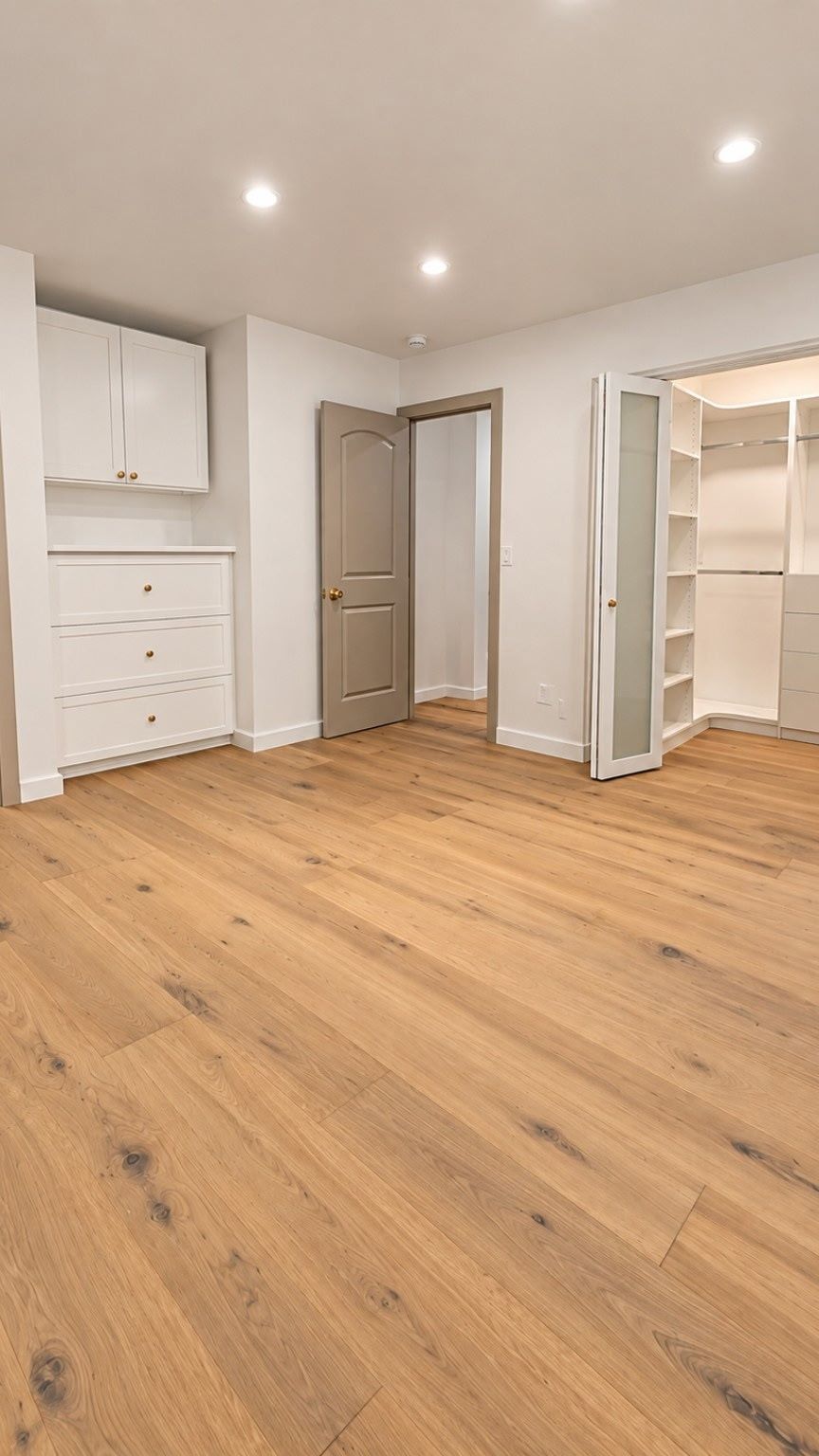 Empty bedroom with light wood floors, white walls, recessed lights, and open bedroom and walk-in closet doors