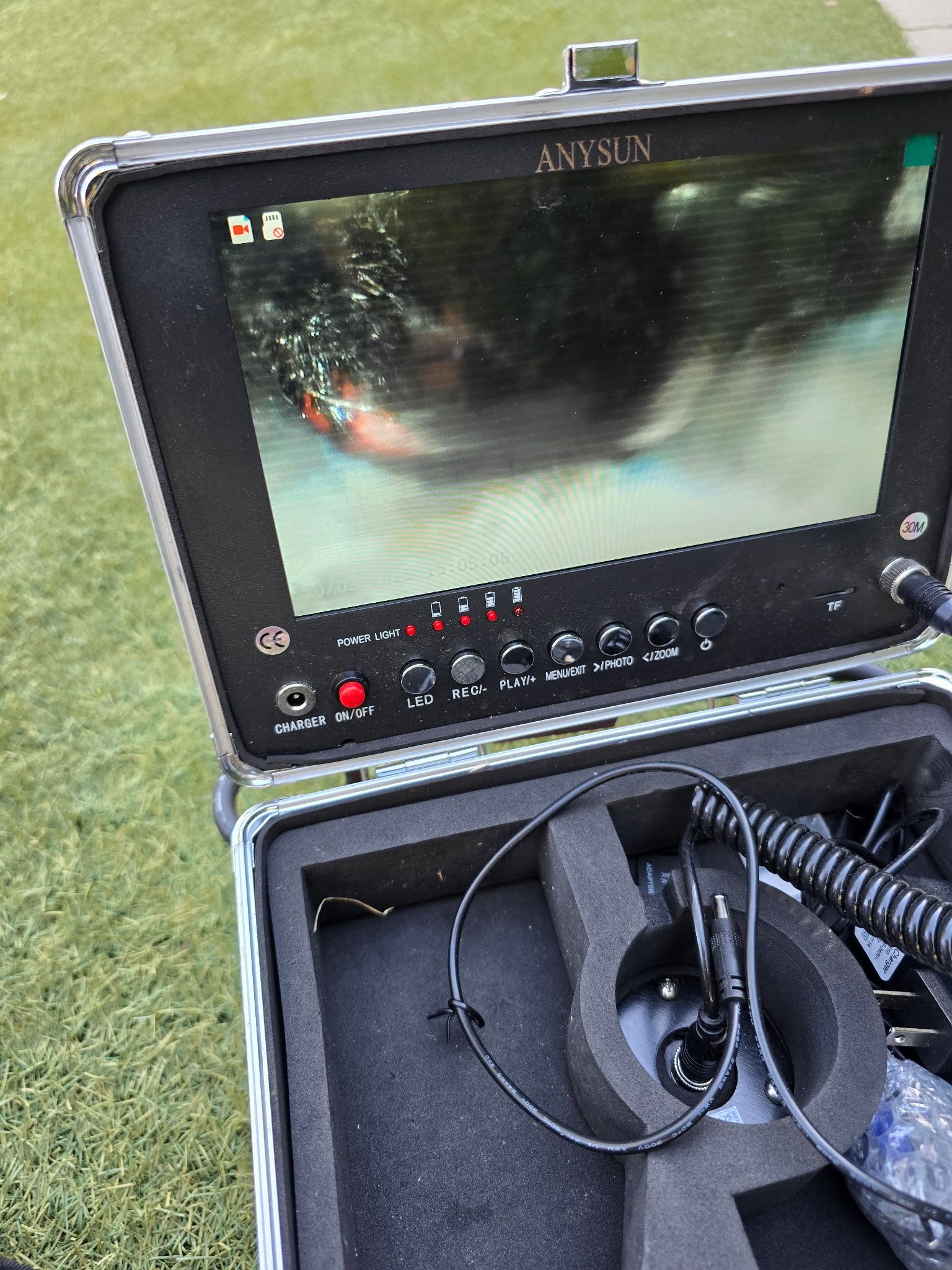 A portable sewer camera monitor in a hard case, displaying a live-feed view inside a pipe on its screen.